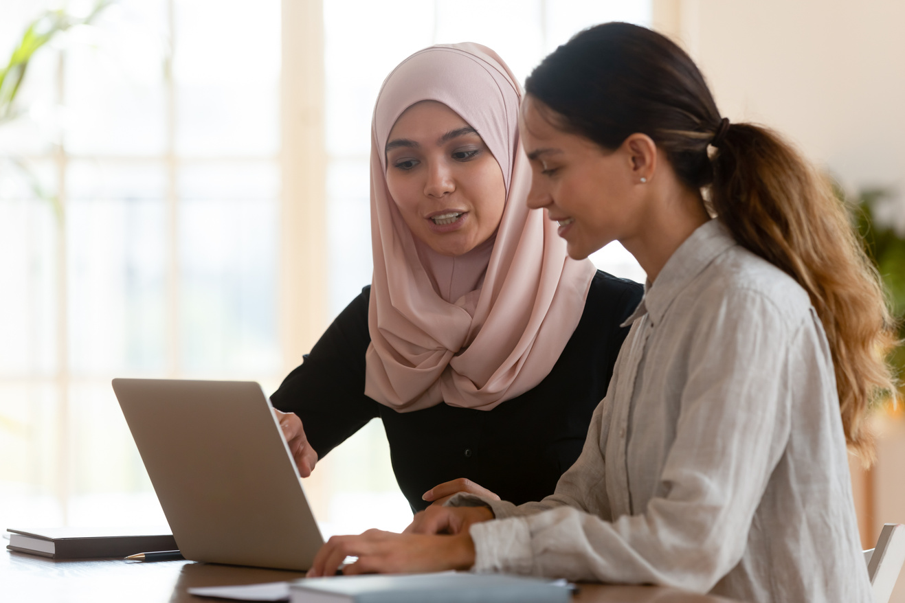Asian muslim female mentor teaching caucasian intern explaining computer work